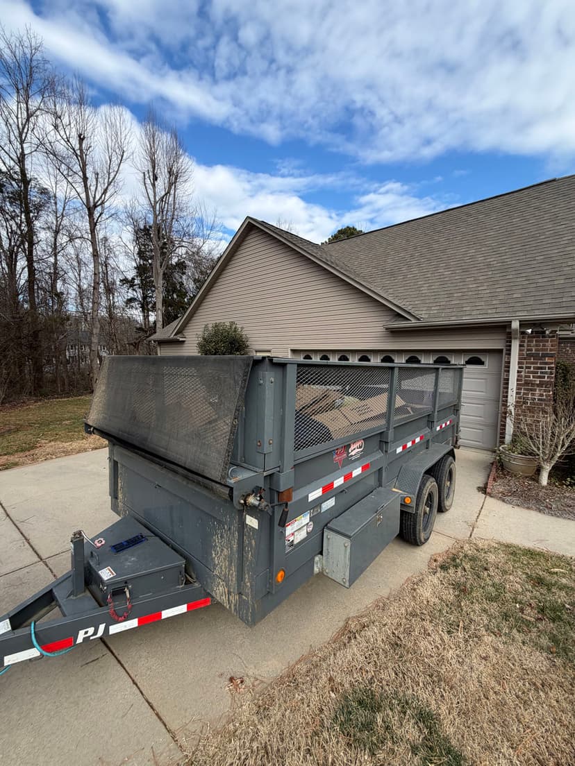 Dump trailer parked in a residential driveway with cloudy sky and trees in the background.